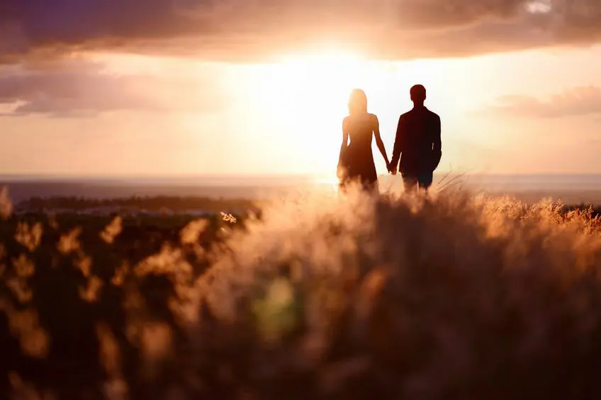 A man and woman holding hands in front of the sun.