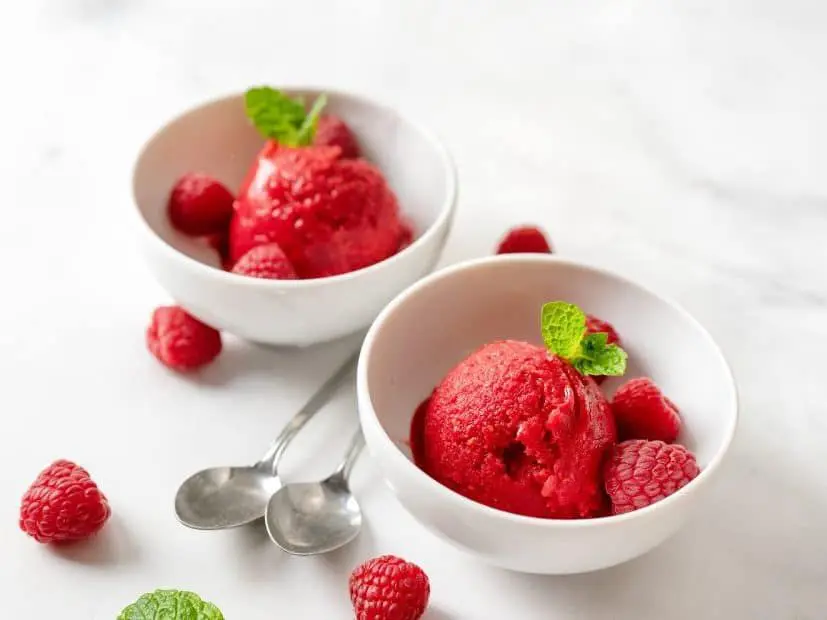 Two bowls of raspberries and ice cream on a table.