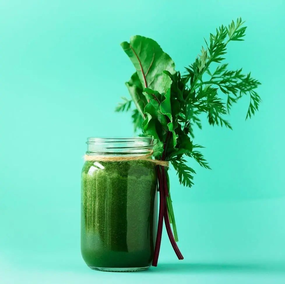 A jar of green juice with leafy greens in it.