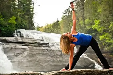 A woman is doing yoga on the rocks near a waterfall.