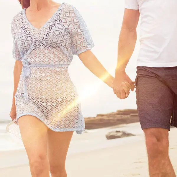 A man and woman holding hands on the beach.