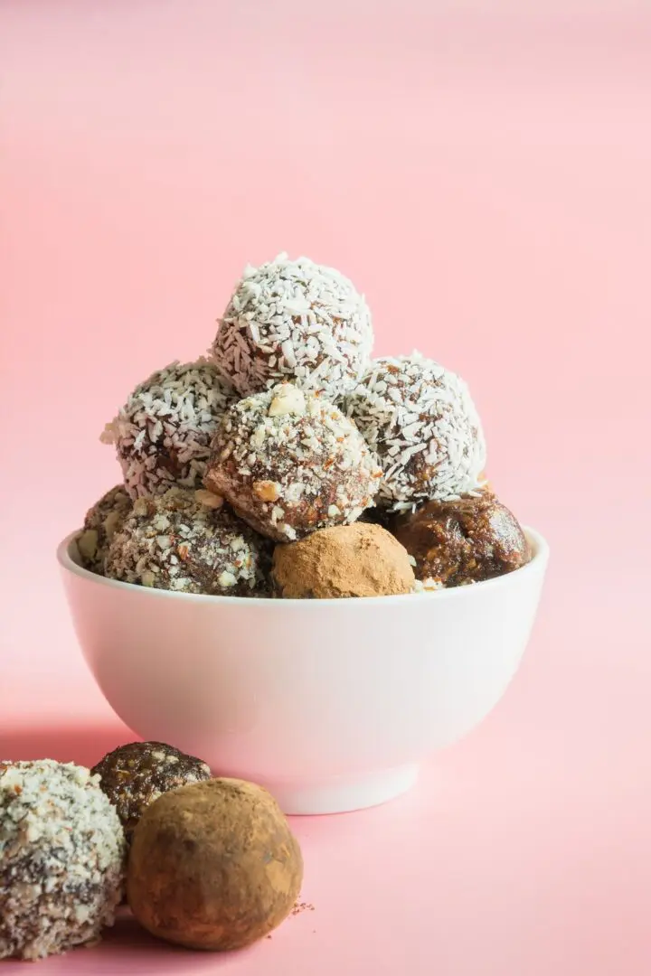 A bowl of cookies and other treats on top of pink background.