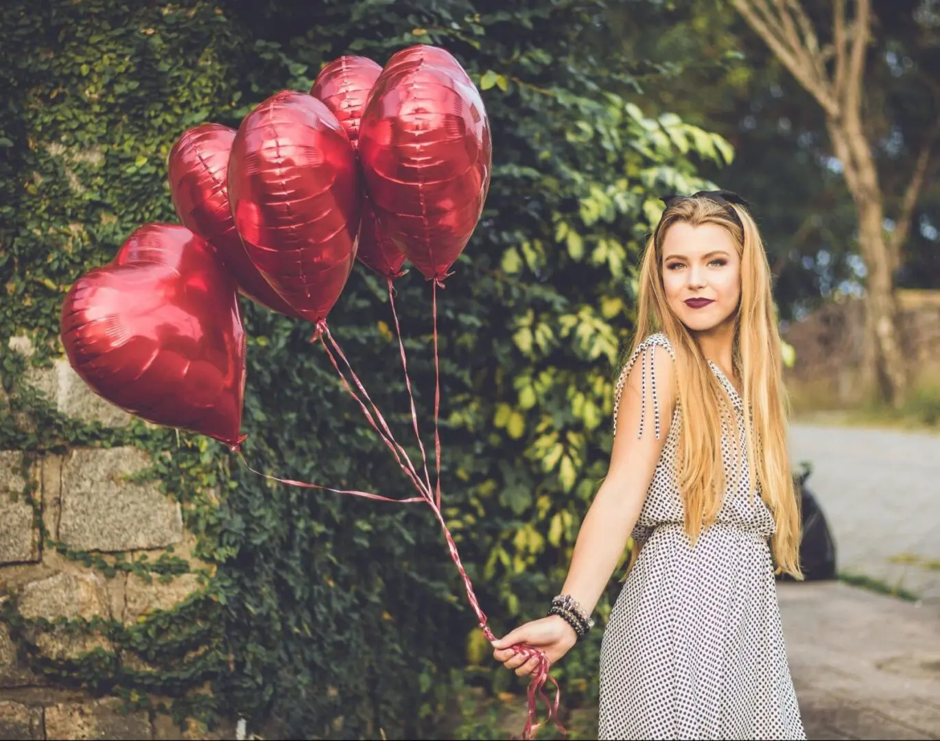A woman holding onto some red balloons