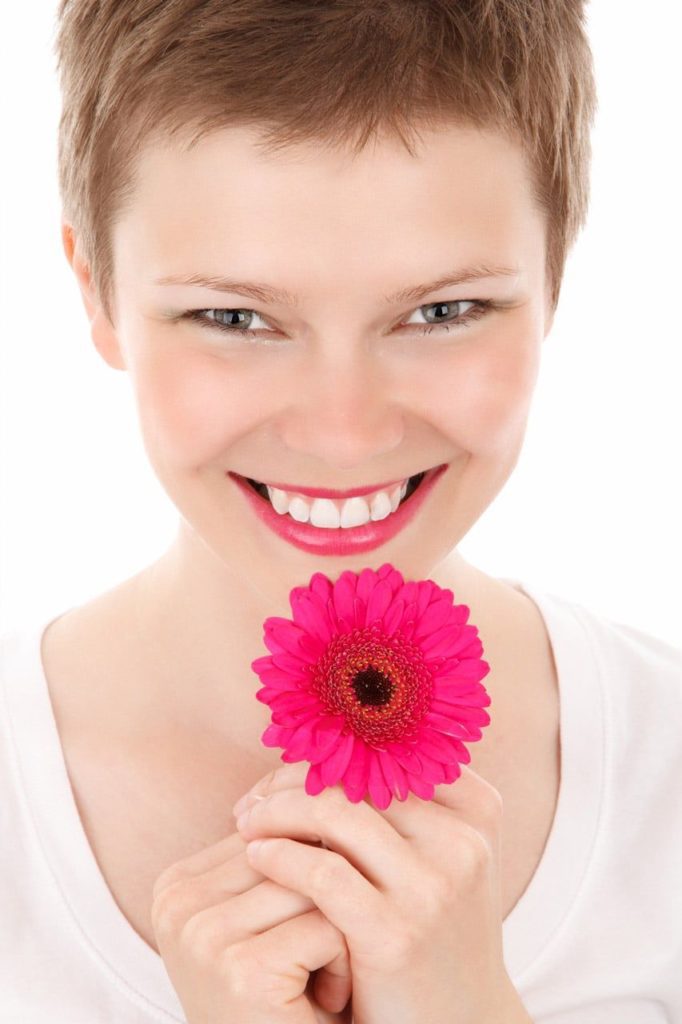 A woman holding a pink flower in her hand.