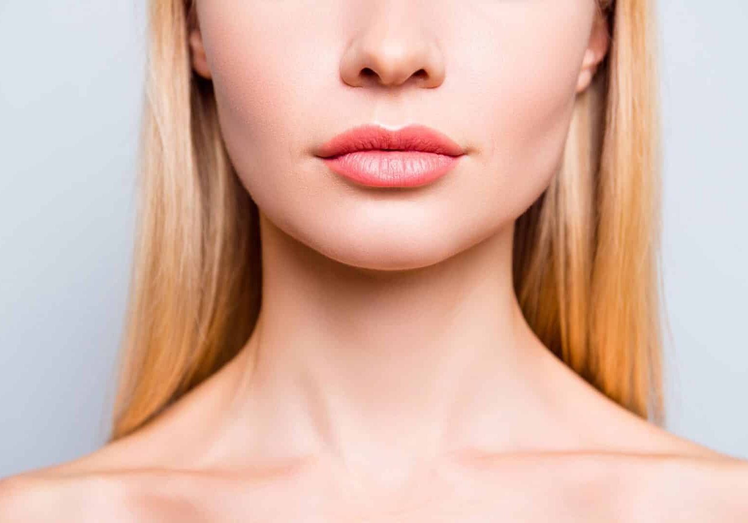 Close up cropped photo of attractive woman's lips without lipstick and after having shape correction, she has expression wrinkles. She is isolated on grey background