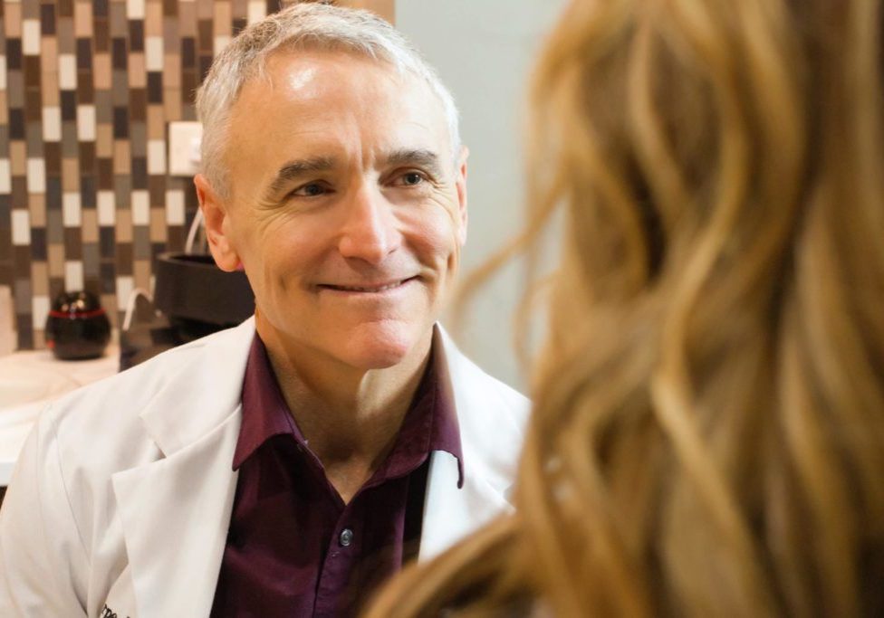 A man in white jacket looking at woman in brown shirt.