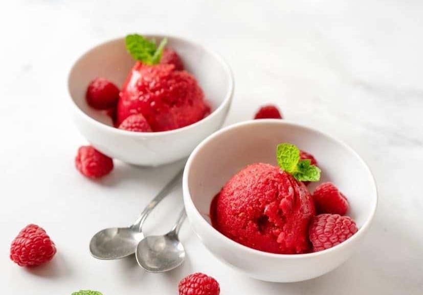 Two bowls of raspberries and ice cream on a table.