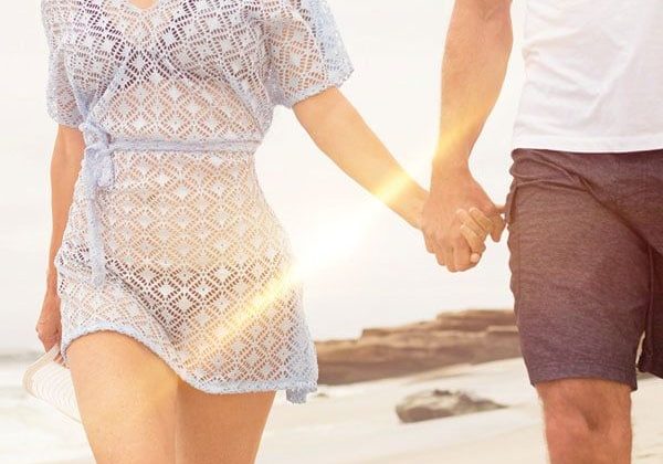 A man and woman holding hands on the beach.