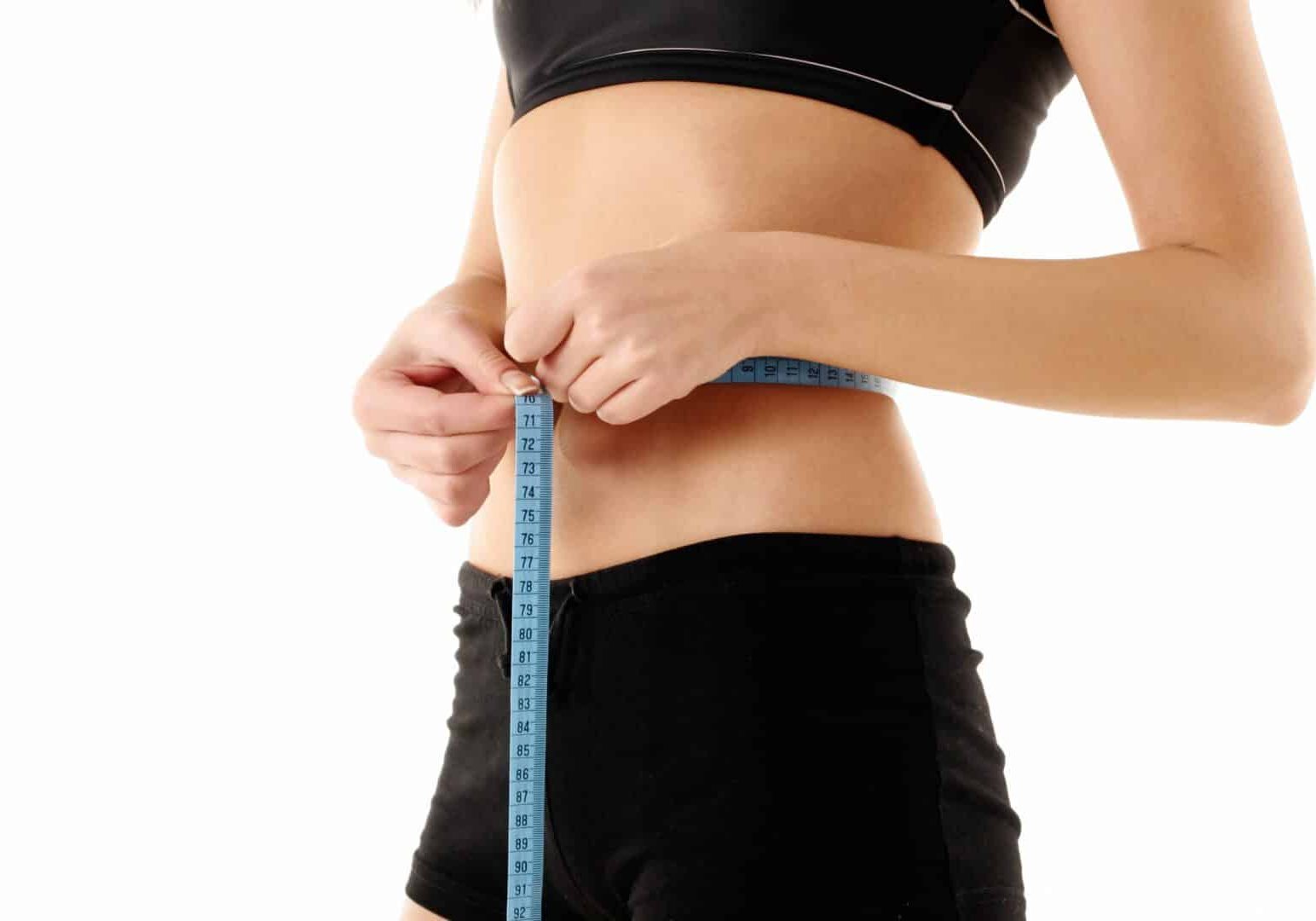 A woman is measuring her waist with a tape measure.
