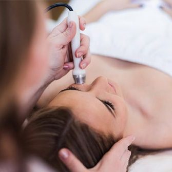 A woman getting her face cleaned with an electric device.
